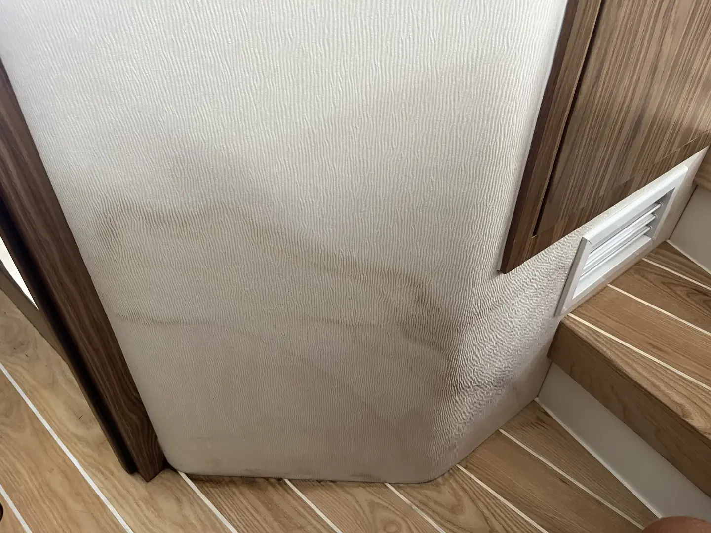 Contact Us Today Stained beige wall panel beside wooden staircase with vent, showing water damage or mold discoloration