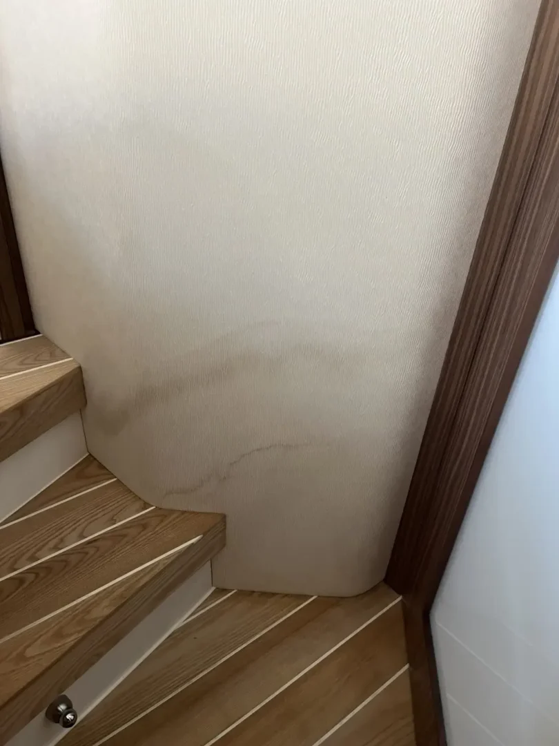 Contact Us Today Corner wall with water stains extending from wooden stairs showing signs of water damage.