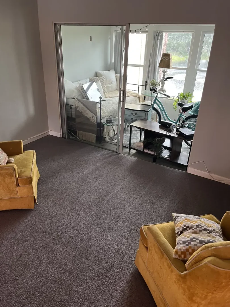 How Did Professional Carpet Cleaning Restore This Home in Dunedin, FL? Carpeted living room with mustard armchairs and glass doors opening to a sunroom with a daybed and bicycle